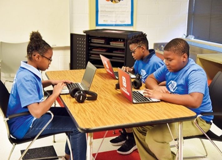 three kids on computers in a classroom